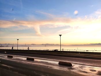 Street by sea against sky during sunset