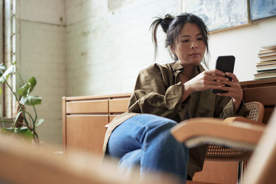 Artist sitting on chair using smart phone in workshop