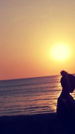 Silhouette man standing on beach against orange sky