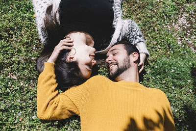 High angle view of romantic couple looking at each other while lying on grassy field in park during sunny day