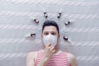 Directly above portrait of man wearing mask lying on bed with bottles