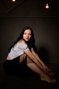 Portrait of seductive woman sitting against wall in darkroom