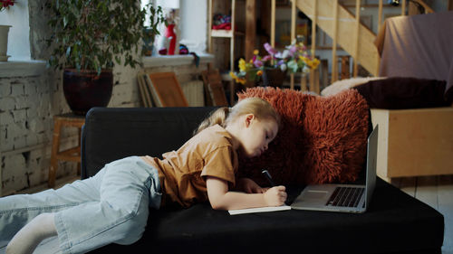 Cute girl studying while lying on sofa at home