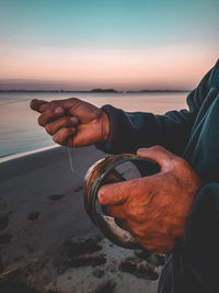 Man holding sand at beach against sky during sunset