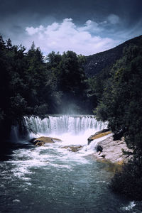 Scenic view of waterfall in forest against sky