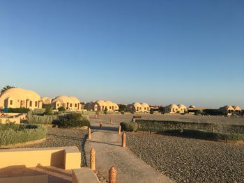 Footpath leading towards houses against clear blue sky