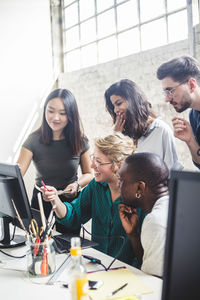 Smiling computer hackers discussing over desktop pc in creative office