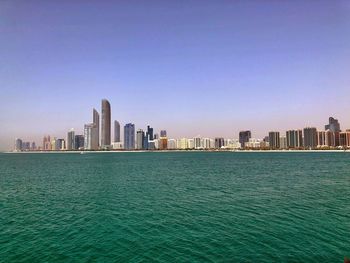 Sea by modern buildings against clear sky