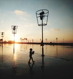 Silhouette boy playing basketball against sky during sunset