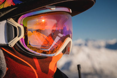 Ski goggles with reflection of snow-capped mountains. a man on a ski slope stands in profile and