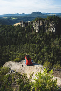 Rear view of people sitting on rock by mountain
