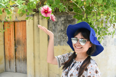 Portrait of smiling young woman wearing hat while standing against wall