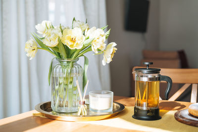 Beautiful bouquet of yellow tulips in vase on dinner table in white kitchen light interior at home