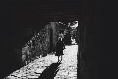 Rear view of senior woman walking with cane in tunnel on sunny day