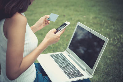 Midsection of mid adult woman doing online shopping while sitting on grassy field