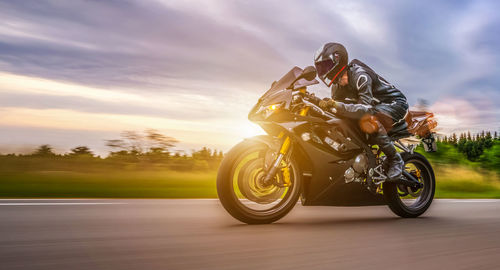 Blurred motion of man riding motorcycle on road against cloudy sky