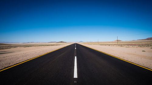 Road passing through landscape against clear blue sky