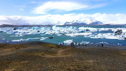 People by glaciers in lagoon against blue sky