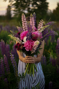 Midsection of woman holding pink flowering plant on field