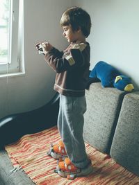 Full length of boy photographing through camera while standing on sofa at home