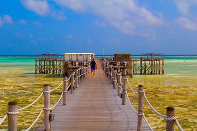 Scenic view of person walking on jetty against cloudy sky