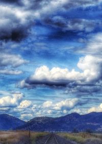 Country road leading towards mountains against cloudy sky