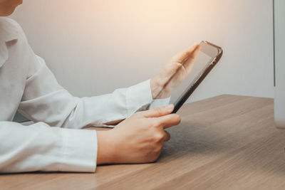 Midsection of man holding mobile phone while sitting on table