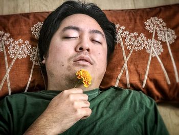 Close-up portrait of man lying down and holding yellow marigold flower.