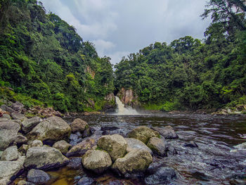 Stream flowing through rocks against sky