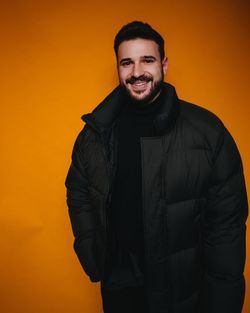 Portrait of smiling bearded man wearing warm clothing while standing against colored background