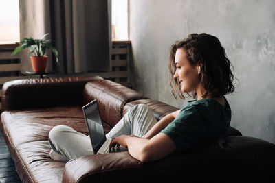 Side view of woman using laptop while sitting on sofa at home