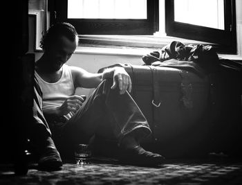 Full length of happy man sitting with drink by window at home