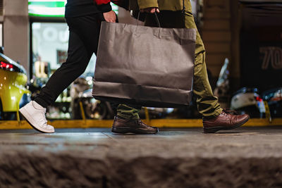 Two people walking through the city at night, one carrying a large shopping bag.