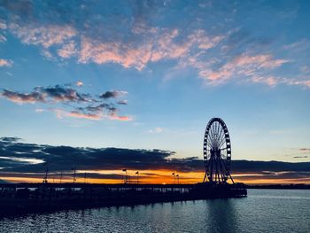 Ferris wheel by sea against sky during sunset