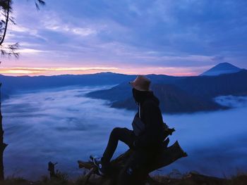 Silhouette man sitting against mountain against sky during sunset