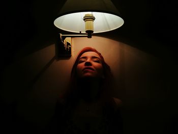 Close-up of woman with eyes closed below light in darkroom