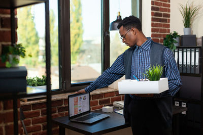 Side view of young woman using digital tablet while standing by window