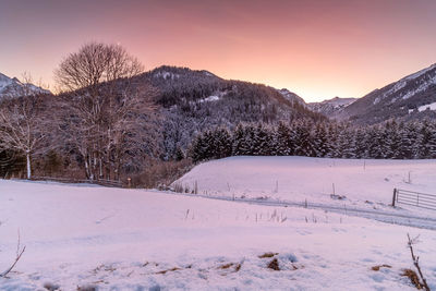 Snow covered field against sky during sunset