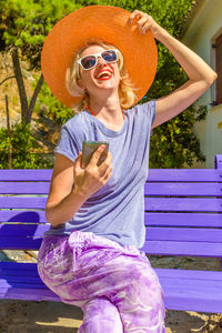Cheerful woman sitting on bench during sunny day