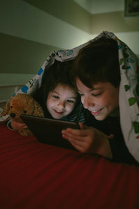 Siblings using digital tablet on bed in darkroom