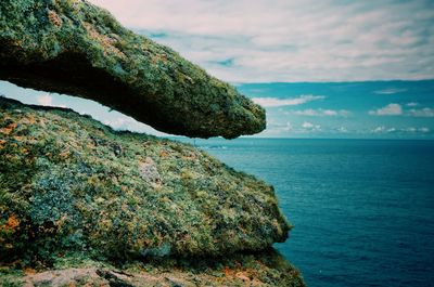 Cliff by sea against cloudy sky