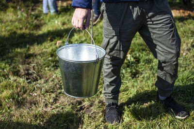 Low section of man holding bucket while standing on field