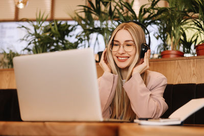 A smiling student wearing glasses and headphones works and studies online using wireless technology