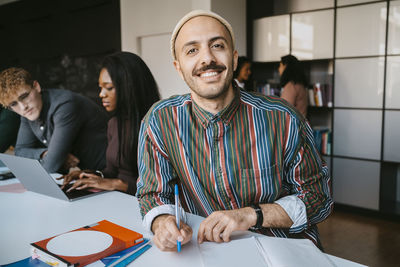 Portrait of smiling male student sitting with book at community college