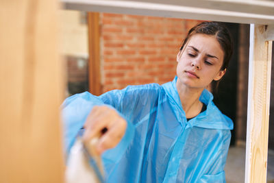 Portrait of young woman standing against window