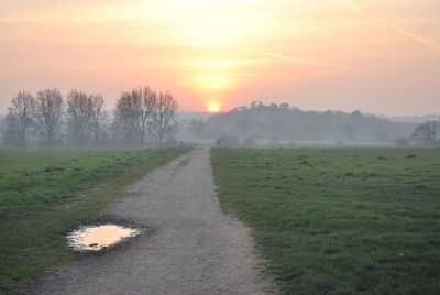 Road amidst field against sky during sunset