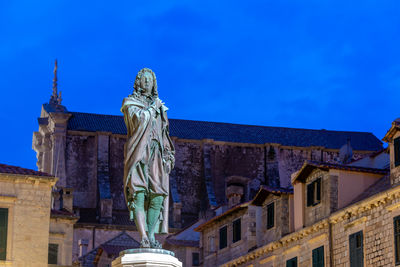 Low angle view of statue against building against blue sky