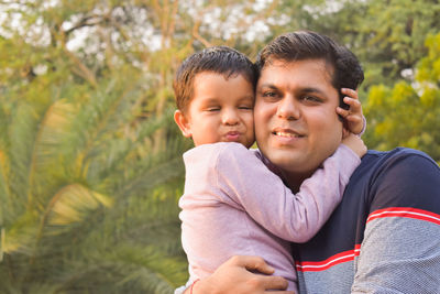 Father carrying cute son against trees