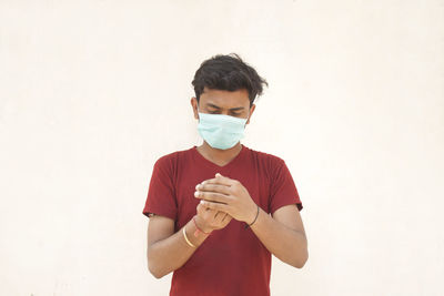 Young man wearing flu mask using hand sanitizer standing against white background