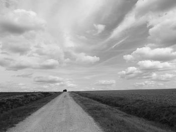 Empty road amidst field against sky